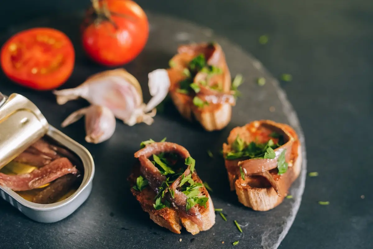 Anchovy fillets on toasted bread with tomato and parsley beside an open tin