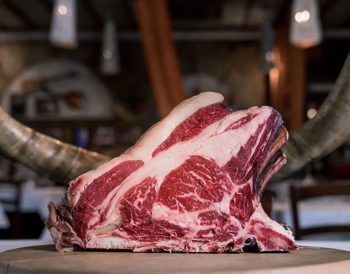 Thick bone-in rib of marbled raw beef standing on a wooden board