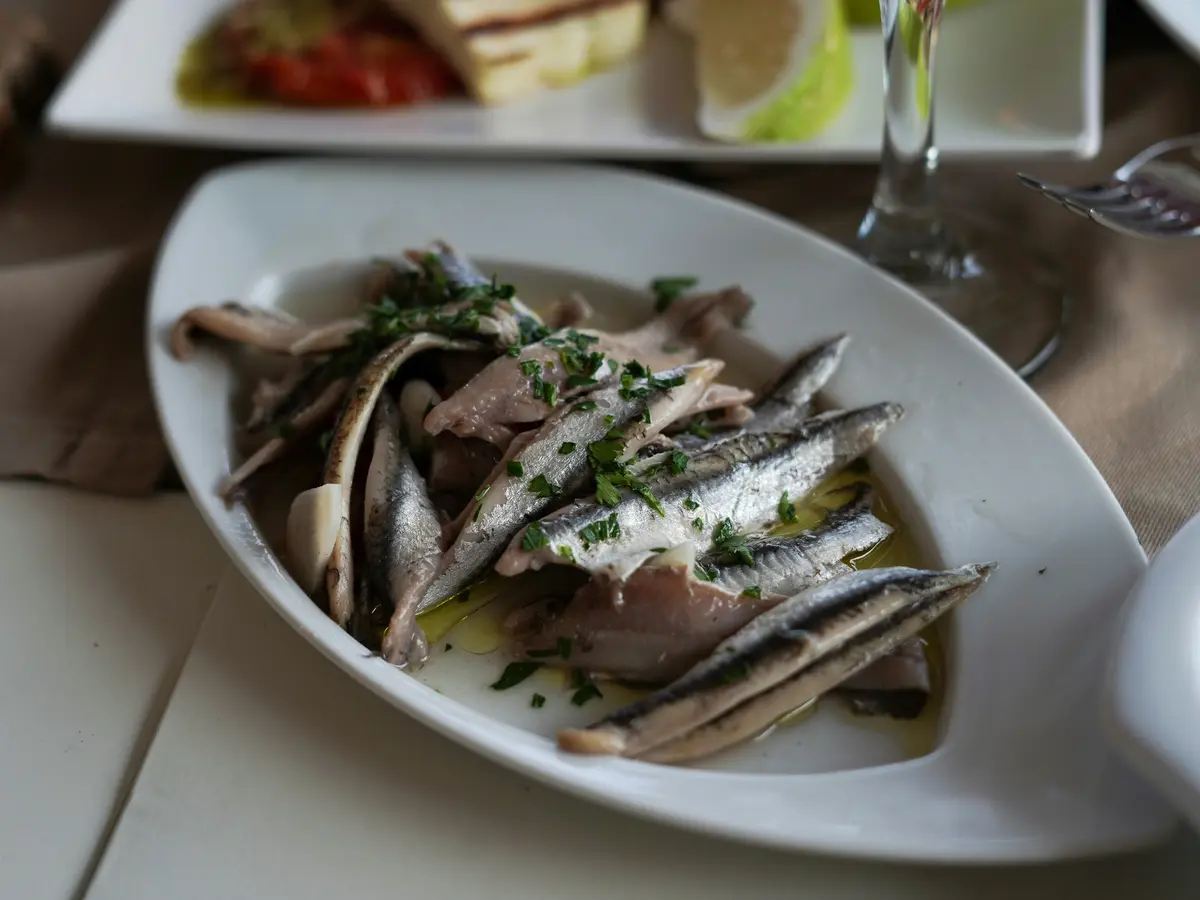 White anchovy fillets marinated in vinegar with garlic, parsley and olive oil on a white dish