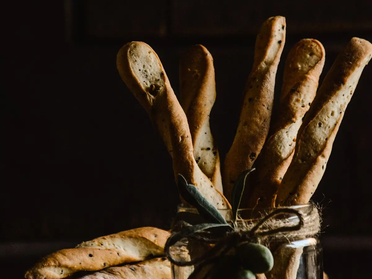 Rustic breadsticks standing in a glass jar tied with twine and an olive sprig