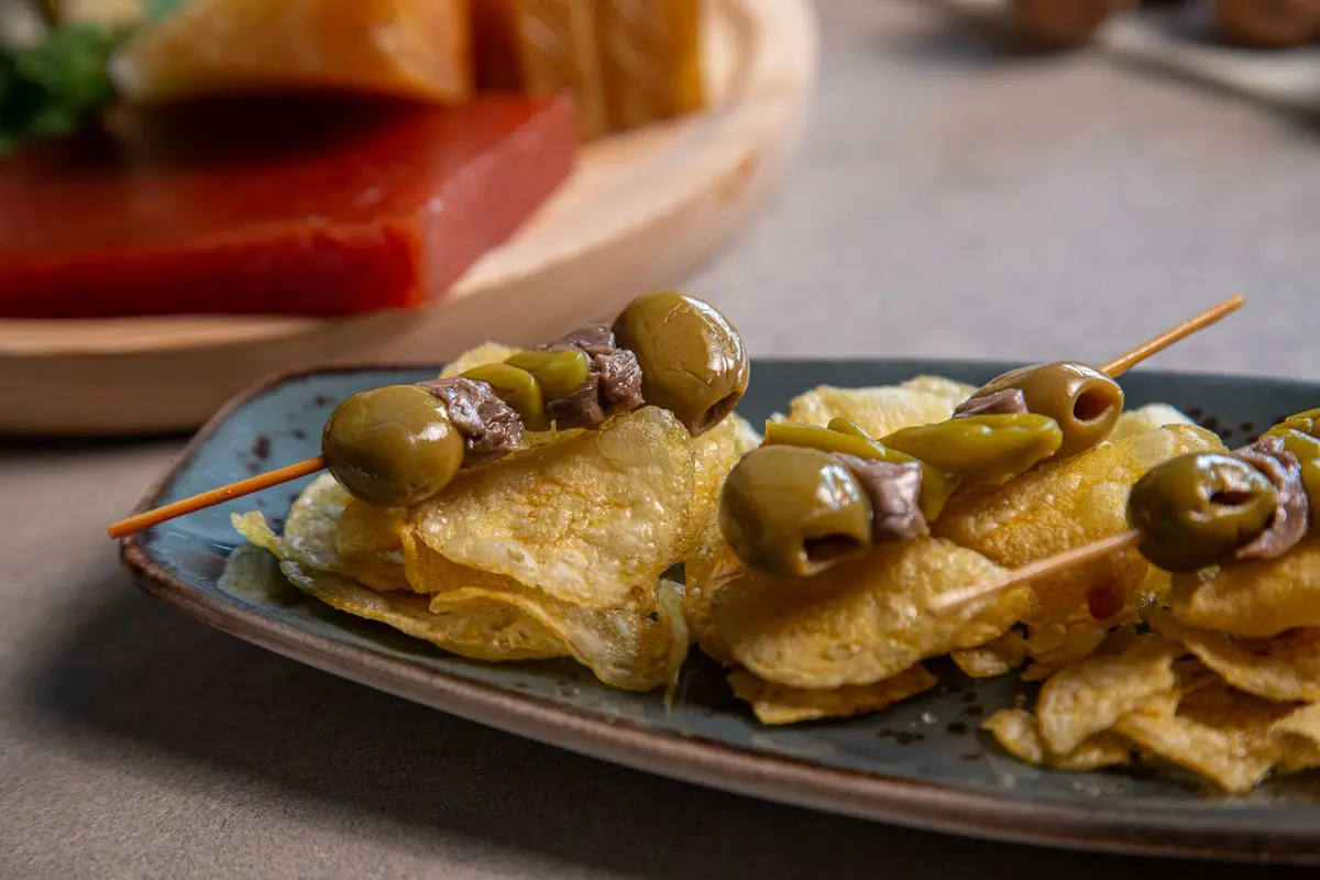 Skewers of olive, anchovy and green pepper on a plate of crisps
