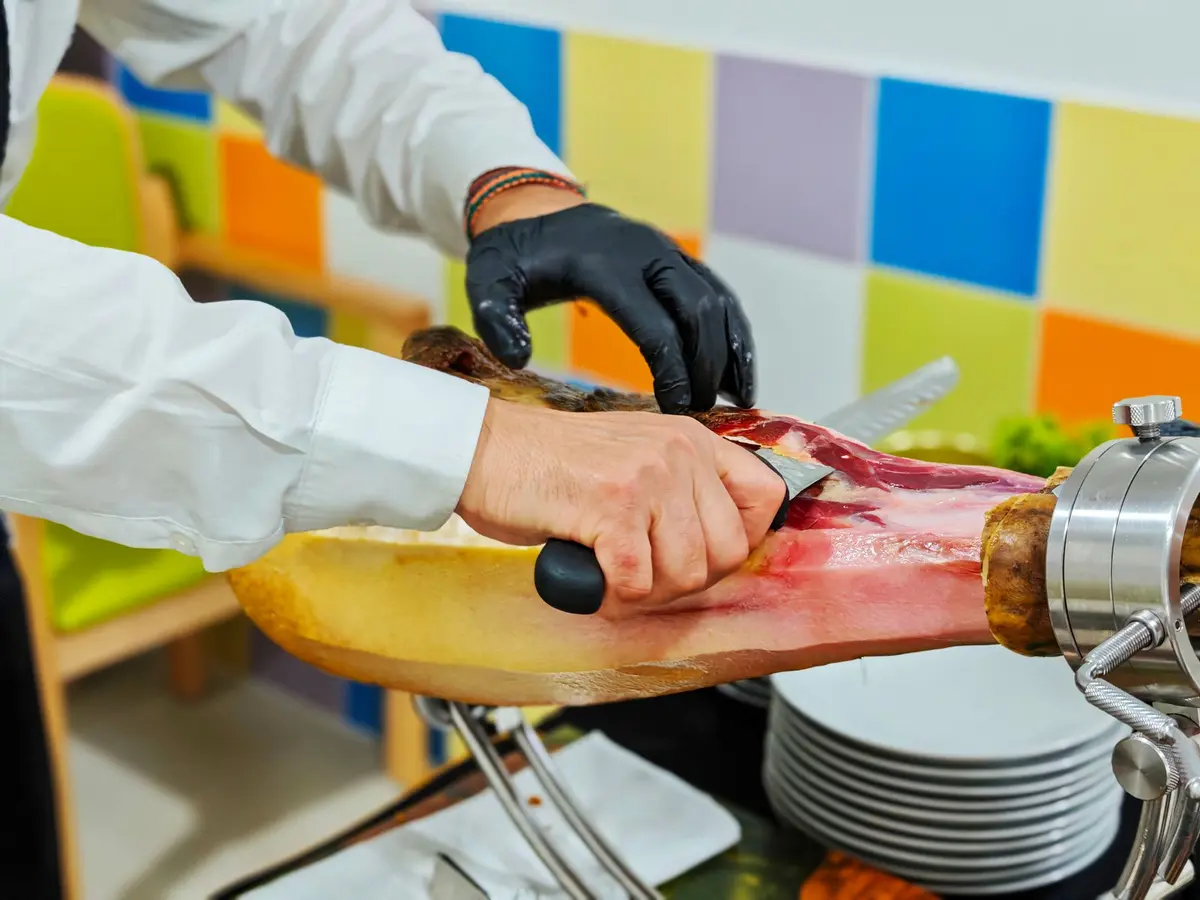 Hand-carving thin slices from a whole cured ham leg held in a ham stand