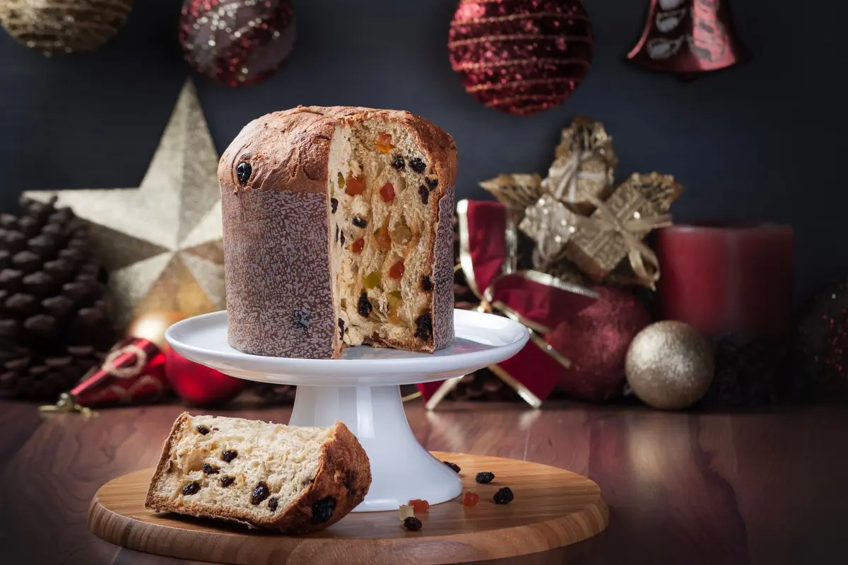 Panettone on a cake stand with a slice cut, festive decorations behind