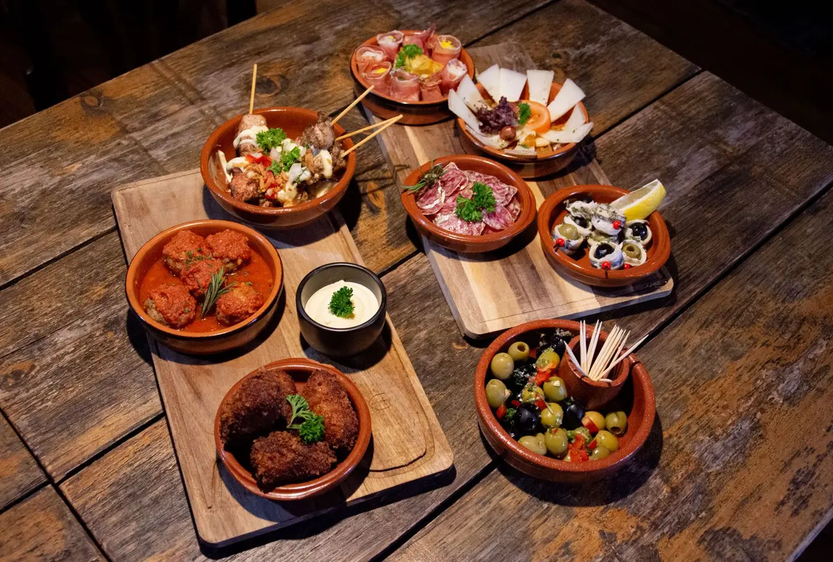 Spread of Spanish tapas in terracotta dishes on wooden boards
